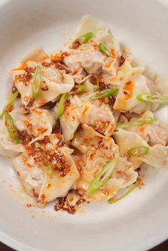 a white plate topped with dumplings covered in sauce and seasoning next to a fork