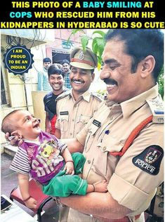 a police officer holding a baby in his lap and smiling at the camera with other officers behind him