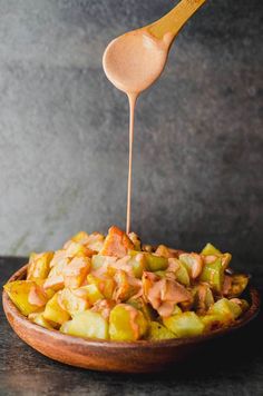 a wooden spoon drizzling sauce onto a dish filled with potatoes and vegetables