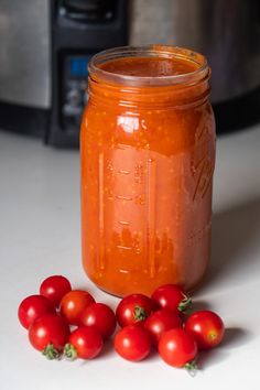 a jar filled with tomato sauce sitting on top of a counter next to some tomatoes