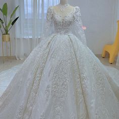 a white wedding gown on display in a room with yellow chair and window behind it