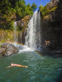 a person swimming in the water near a waterfall