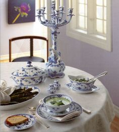 a white table topped with blue and white dishes filled with food next to a candelabra