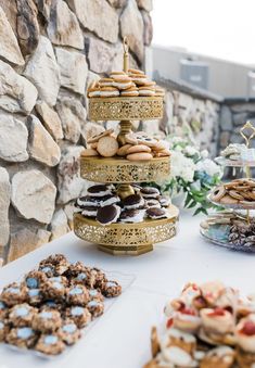 a table topped with lots of different types of cookies and pastries next to a stone wall