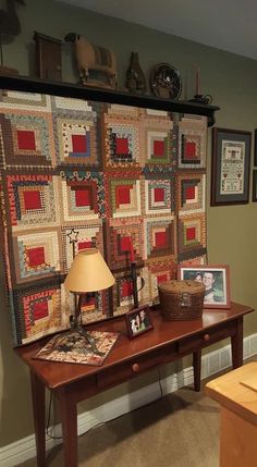 a table with a lamp on top of it in front of a wall hanging quilt