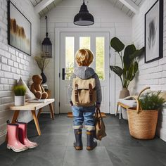 a young boy with a backpack and boots walking into a room filled with potted plants