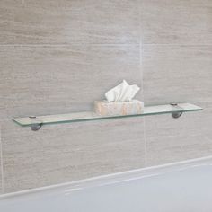 a glass shelf on the wall above a bathtub filled with toilet paper and tissue