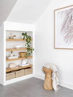 a white room with shelves and baskets on the floor next to a potted plant