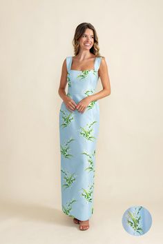 a woman standing in front of a white wall wearing a blue dress with green plants on it