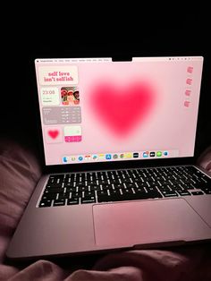 an open laptop computer sitting on top of a pink bed cover covered in sheets and pillows