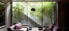 a living room filled with furniture next to a window covered in bamboo trees and plants