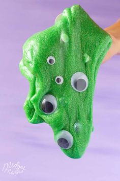 a green object with googly eyes hanging from it's side on a purple background