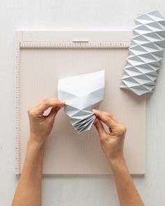 two hands are holding up some paper on top of a piece of art work that looks like origami