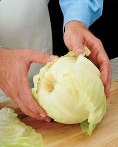 a person cutting up cabbage on top of a wooden cutting board