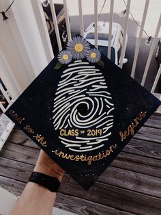 a hand holding a graduation cap that has a fingerprint on it and daisies