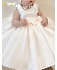 a baby girl wearing a white dress with a bow