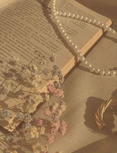 an open book with pearls and flowers on it next to a string of bracelets