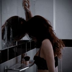 a woman standing in front of a bathroom mirror brushing her long hair with an electric razor