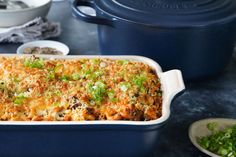 a blue casserole dish with green onions and cheese on top, next to other dishes