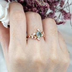 a close up of a person's hand with a ring on their finger and flowers in the background