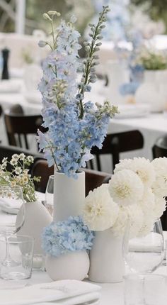 a table set up with white and blue flowers in vases, plates and napkins