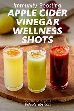 three glasses filled with liquid sitting on top of a wooden cutting board next to fruit