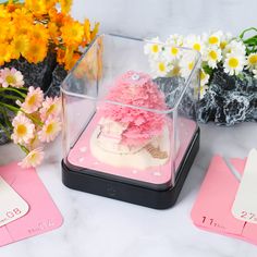 there is a cake in a glass case on the table next to flowers and cards