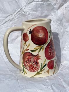 a ceramic pitcher with pomegranates painted on it's side and sides