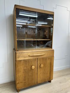 a wooden cabinet with glass doors on the top and bottom, in front of a white wall