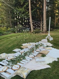 a long table set up with plates and place settings for an outdoor dinner in the woods