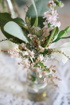 a vase filled with flowers and greenery on top of a white tablecloth covered table