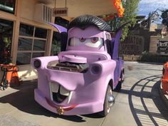 a purple car with an evil face on it's hood parked in front of a building