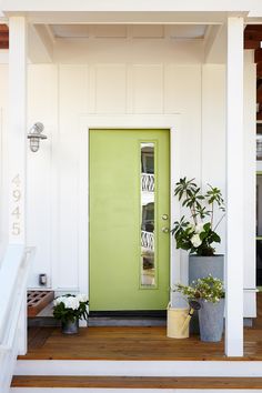 a green door on the side of a white house with potted plants in front