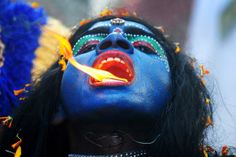 a woman with blue paint on her face and head is holding a yellow object in her mouth