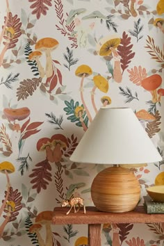 a lamp sitting on top of a wooden table next to a wall covered in flowers