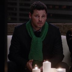 two people sitting on a couch with candles in front of them and one person wearing a green scarf