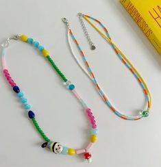 two necklaces are sitting on a table next to a yellow book and some beads