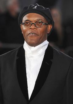 an older man wearing glasses and a black hat is looking at the camera while standing in front of a crowd