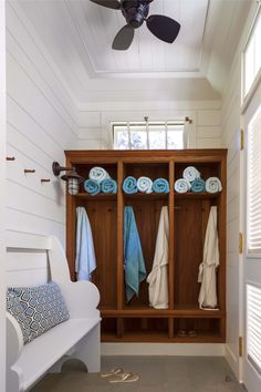 a white bench sitting under a window next to a wooden shelf filled with blue towels