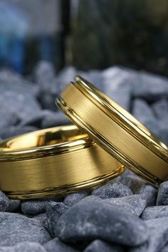 Close-up of two gold rings with a brushed finish, resting on smooth grey pebbles. The rings feature polished edges and interiors, highlighting their luxurious and sophisticated design against a natural stone background. Engraved Wedding Bands, Laser Engraved Wedding, Wedding Band Engraving, Tungsten Rings, Engraved Wedding, Stylish Rings, Tungsten Ring, Laser Engraved, Gold Finish