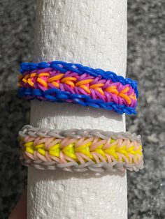 two different colored bracelets on top of a white paper towel holder in front of a granite countertop