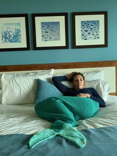 a woman laying on top of a bed under a green mermaid tail knitted blanket