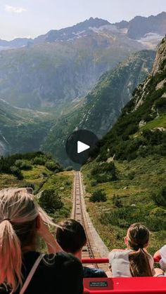 people are sitting on a bench looking at the mountains and valleys in the distance, with a train track running through them