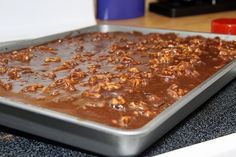 a pan filled with chocolate and nuts on top of a counter next to a blue cup