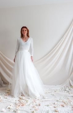 a woman in a white wedding dress standing on a bed with flowers all over it