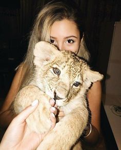 a woman is holding a baby tiger in her arms while she looks at the camera