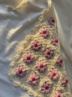 a crocheted doily with pink and white flowers is laying on a bed