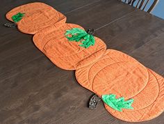 an orange pumpkin shaped table runner with green leaves on the top and bottom, sitting on a wooden floor