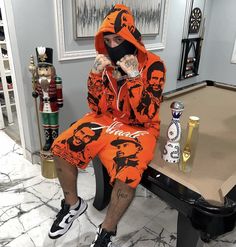 a man sitting on top of a pool table wearing an orange sweatshirt and sweatpants