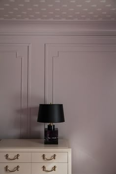 a lamp on top of a dresser in a room with pink walls and white furniture